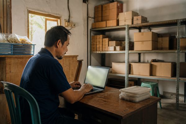 Pemilik usaha kecil menyiapkan daftar pekerjaan berulang di meja kerja sambil membuka laptop