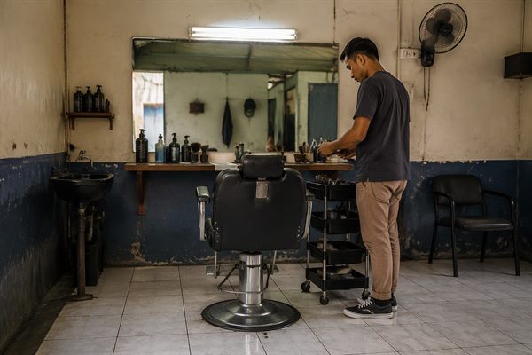 Kursi salon berhadapan dengan cermin besar dan meja berisi alat potong rambut